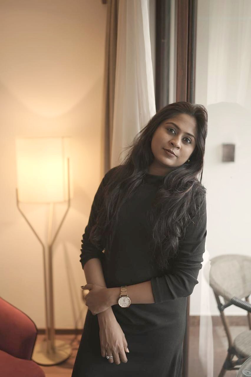 Dr. Aiswaryia Mohan in black, standing by a warm lamp
